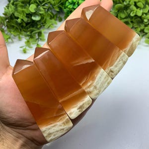May include: Six orange calcite crystal points with white banding. The points are arranged in a row, with the largest point at the top and the smallest point at the bottom.