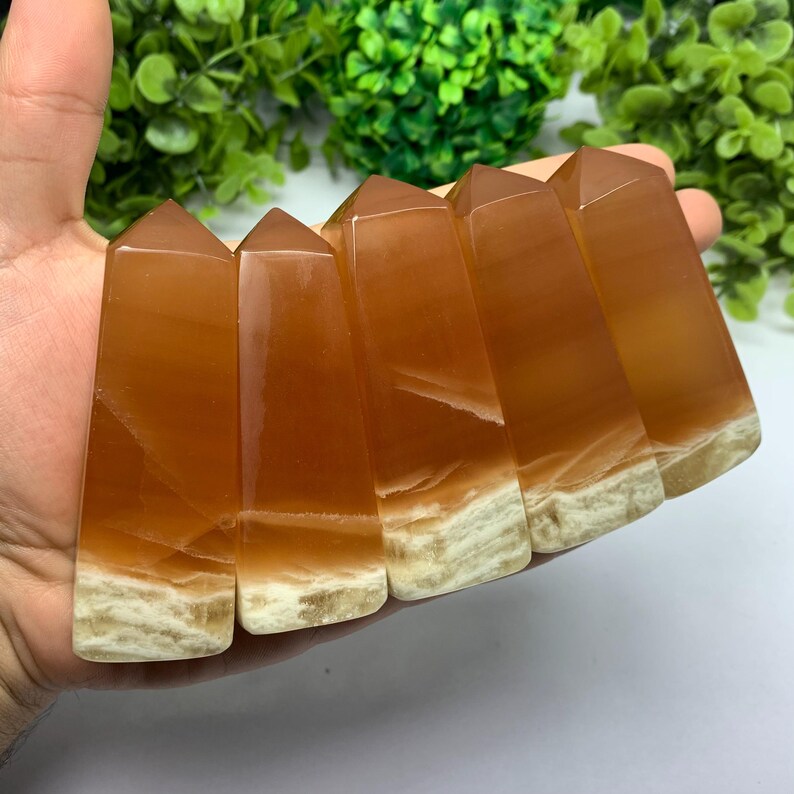 May include: Six orange and white calcite crystal points, also known as Mexican onyx, are arranged in a row. The points are polished and have a smooth, glassy finish.