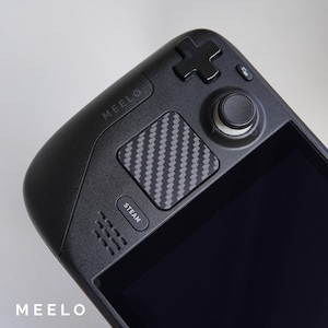 May include: A black handheld gaming device with a carbon fiber texture on the top. The device has a black screen, a black d-pad, and a black button labeled "STEAM". The device also has the word "MEEELO" printed on the top.