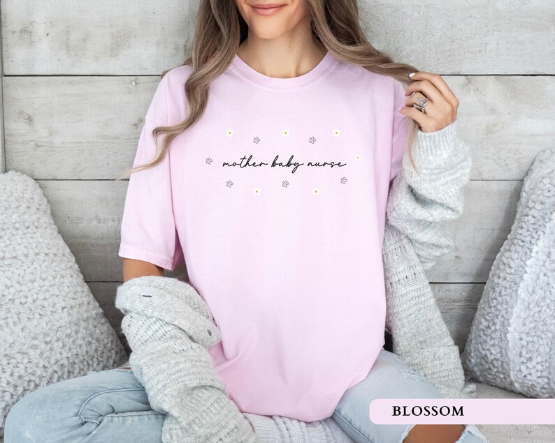 Soft pink blossom aesthetic postpartum nurse shirt worn by a sitting model, featuring an elegant floral design.
