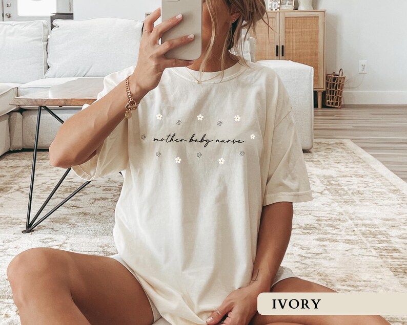 Woman modeling an ivory oversized Comfort Colors tee highlighting the beautiful floral mother baby nurse design, perfect for a work outfit.