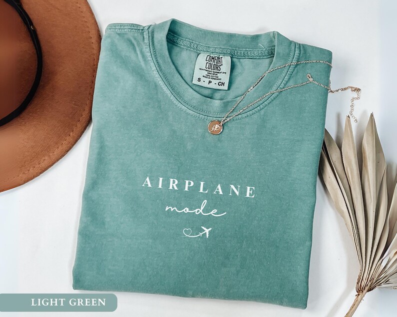 May include: Light green t-shirt with the text "AIRPLANE mode" in white lettering and a small airplane graphic. The shirt is made of a soft, comfortable material.