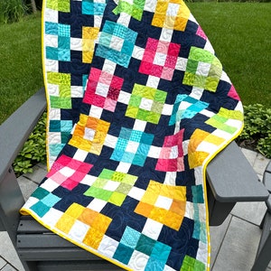 May include: A colorful patchwork quilt with a black and white background. The quilt is made up of squares of different colors and patterns, including yellow, green, blue, pink, and red. The quilt is edged with a yellow border.