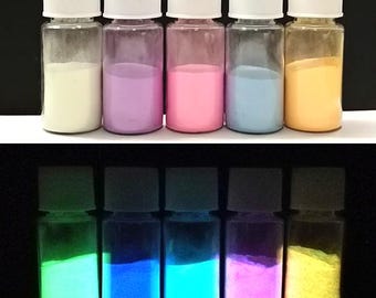 May include: Six small glass bottles with white lids containing different colored glow-in-the-dark powders. The powders are white, purple, pink, blue, and orange in the top row and green, blue, green, pink, and yellow in the bottom row.