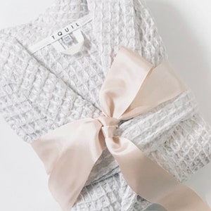 May include: A grey waffle weave robe with a white satin ribbon tied in a bow. The robe has a label that says "TQUIL" on it.