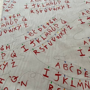 May include: White fabric with red letters spelling out the alphabet in a repeating pattern. The letters are strung together with a string of lights. The letters are dripping with blood.