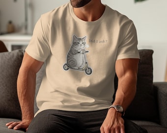 May include: Beige t-shirt featuring a cartoon cat riding a scooter. The cat is gray and white with a grumpy expression. The text "Did I ask?" is above the cat. The shirt is a neutral color.