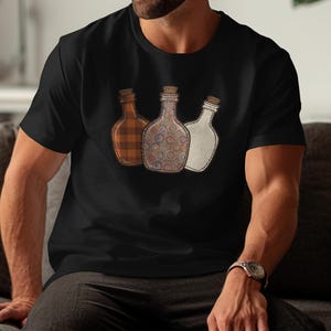 May include: Black t-shirt with three decorative bottles with cork stoppers. The bottles have unique designs: one with a plaid pattern, one with a swirl pattern, and one with a stitched outline.