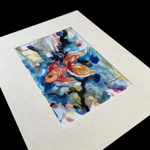 Puede incluir: Pintura acuarela de un pez dorado nadando en un fondo abstracto azul y verde. El pez dorado es naranja y rojo con ojos negros. El fondo es una mezcla de azul, verde, amarillo y rosa.