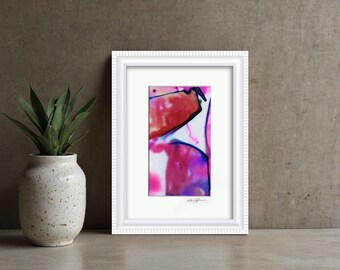 May include: A framed abstract art print featuring vibrant splashes of magenta, red, and deep blue ink on a white background. The artwork is encased in a white, textured rectangular frame with a white mat board and a signature at the bottom.