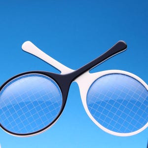 Puede incluir: Gafas de lectura blancas y negras con un patrón de cuadrícula en las lentes. Las gafas están diseñadas para ayudar a leer.