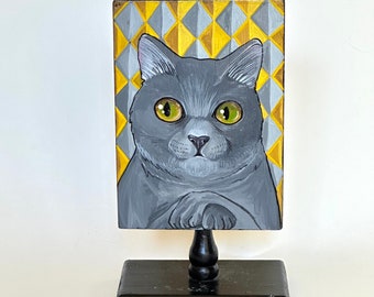 Original painting of chubby gray cat w/ golden eyes and crossed paws against an art deco diamond design in grey and yellow - Acrylic & wood