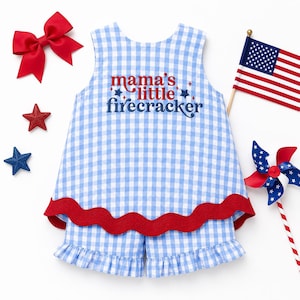 May include: A blue and white gingham baby outfit with the text "mama's little firecracker" embroidered on the front. The outfit includes a sleeveless top and shorts, trimmed with red. Accessories include a red bow, star-shaped decorations, a pinwheel, and a small American flag.