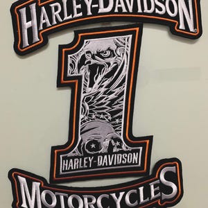 May include: Black and white Harley-Davidson motorcycle patch with an eagle and skull design. The patch has an orange border and the text "Harley-Davidson Motorcycles" in white.