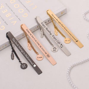 May include: A set of six personalized metal bookmarks with different engraved messages and charms. The bookmarks are black, silver, gold, and rose gold. The charms include a feather, a heart, a lightning bolt, a star, and a small figure.