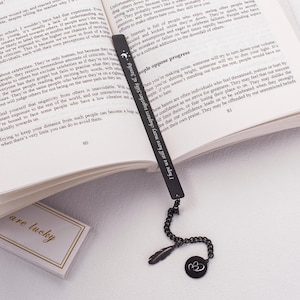 May include: A black metal bookmark with a feather charm and a double heart charm. The bookmark has an inscription that reads "People who love learning are always a joy to be along!"