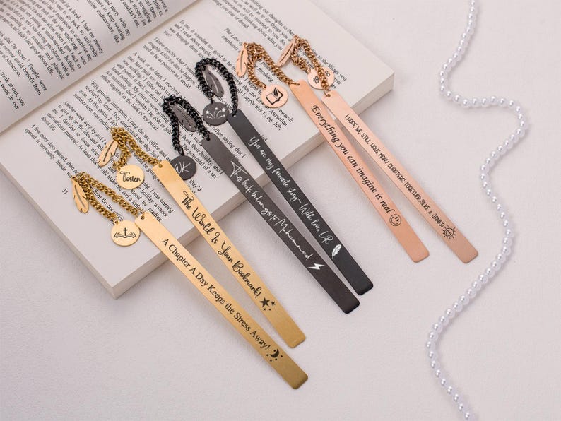 May include: Five gold and black metal bookmarks with different inspirational quotes and designs. The bookmarks feature a feather charm, a cross charm, a star charm, a lightning bolt charm, and a sun charm.