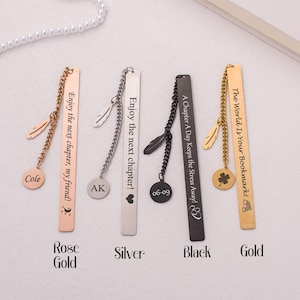 May include: Four metal bookmarks with different colored finishes: rose gold, silver, black, and gold. Each bookmark has a chain with a charm and a personalized inscription. The inscriptions are: "Enjoy the next chapter, my friend!" "Enjoy the next chapter!" "A Chapter A Day Keeps the Stress Away!" and "The World Is Your Bookmark!"