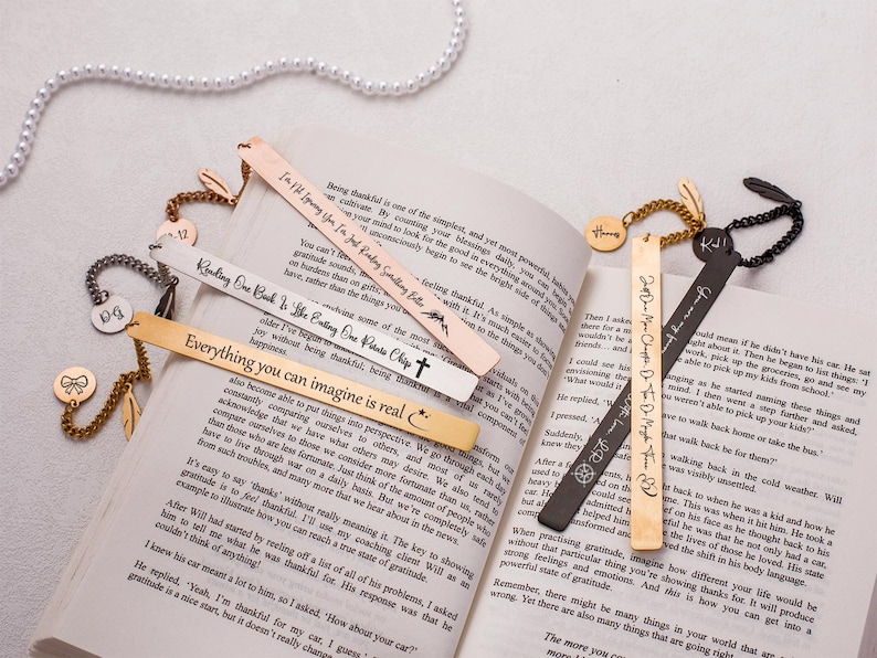 May include: A collection of gold and black metal bookmarks with inspirational quotes engraved on them. The bookmarks are displayed on a book with a white background.