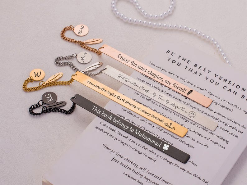 May include: A set of six gold and silver bookmarks with feather accents and personalized inscriptions. The bookmarks feature inspirational quotes and sayings, including "Enjoy the next chapter, my friend!" and "You are the light that shines in every tunnel."