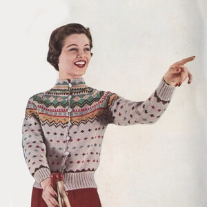 Puede incluir: Una mujer lleva un cárdigan gris claro con un estampado geométrico de colores. El cárdigan tiene cuello alto y cierre de botones. Lleva pantalones rojos y sostiene un bastón.