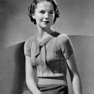 May include: A black and white photo of a woman wearing a knitted sweater with a bow at the neckline. The sweater has short sleeves and a ribbed texture.