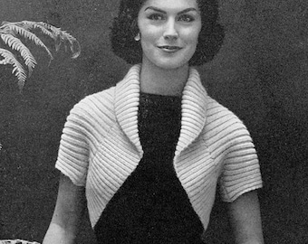 May include: A woman wearing a white knitted cropped cardigan with a wide collar and short sleeves. The cardigan is made of a soft, textured yarn.