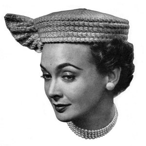 May include: A black and white photo of a woman wearing a crocheted hat with a bow on the side. The hat is a light gray color and has a simple design.