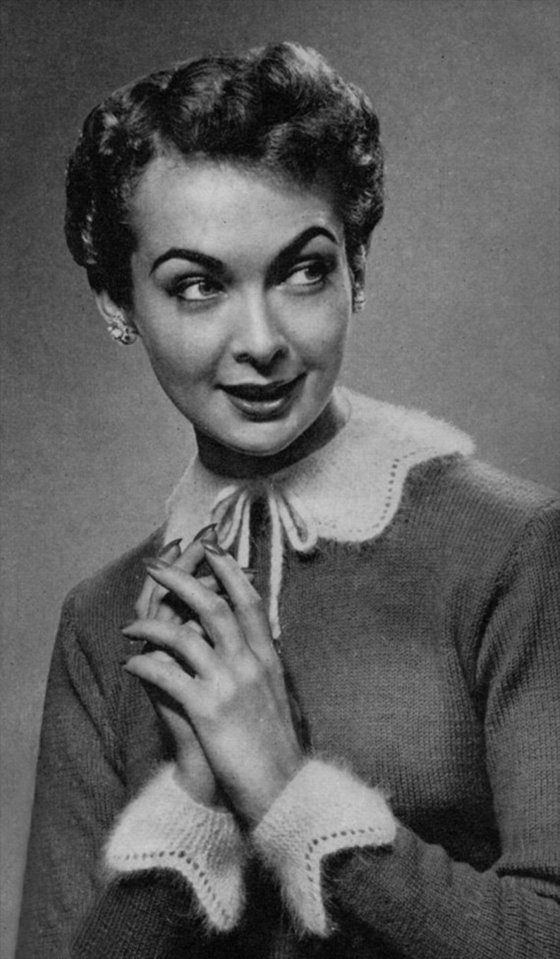 May include: A black and white photo of a woman wearing a knitted sweater with a white collar and cuffs. The sweater has a delicate lace pattern on the collar and cuffs.
