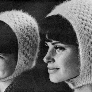 May include: Two women wearing white knitted hats with a lacy pattern. The hats have a long flap that covers the neck and chin.
