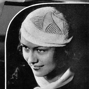 May include: A white crocheted hat with a lacy design. The hat is angled on the head of a person with short, wavy hair. The person is smiling.