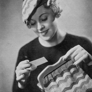 May include: A woman wearing a crocheted hat and a black sweater is holding a crocheted purse with a wooden frame. She is looking at a small white card.