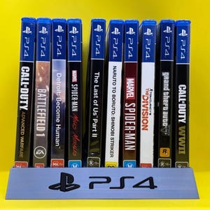 May include: A grey plastic stand with the text "PS4" printed on the front. The stand holds 10 video game cases, all for the PlayStation 4 console. The game titles include "Call of Duty: WWII", "Grand Theft Auto", "The Division", "Marvel's Spider-Man", "Naruto to Boruto: Shinobi Striker", "The Last of Us Part II", "Marvel's Spider-Man: Miles Morales", "Detroit: Become Human", "Battlefield 1", and "Call of Duty: Advanced Warfare".