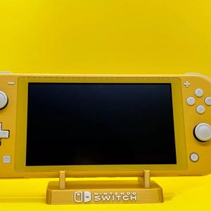 May include: A yellow Nintendo Switch console with a black screen is on a yellow stand. The stand has the Nintendo Switch logo on it.