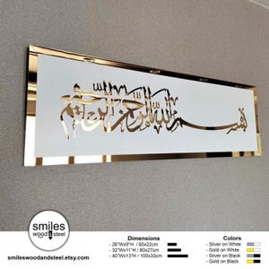 May include: A white rectangular wall art piece with gold Arabic calligraphy. The calligraphy reads "Bismillah Al-Rahman Al-Rahim". The art piece is framed with a gold border. The art piece is available in three sizes: 26 inches by 9 inches, 32 inches by 11 inches, and 40 inches by 13 inches. The art piece is also available in two color combinations: silver on white and gold on white.