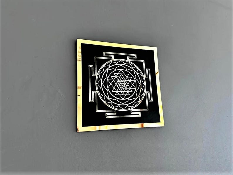 Puede incluir: Un cuadrado negro con marco dorado, que presenta un s&iacute;mbolo Sri Yantra blanco en el centro. El s&iacute;mbolo es un dise&ntilde;o geom&eacute;trico con tri&aacute;ngulos y c&iacute;rculos.