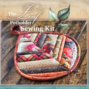 May include: The Leaf Potholder Sewing Kit features a patchwork design with autumnal colors and patterns, including pumpkins, leaves, and plaid. The potholder is made of fabric and has a loop for hanging.