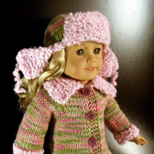 May include: A doll wearing a pink and green striped knitted cardigan with a pink fur trim. The doll is also wearing a pink knitted hat with a fur pom-pom.