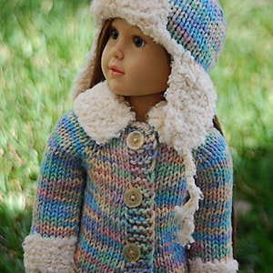 Puede incluir: Una muñeca con un suéter de punto multicolor con ribete de piel blanca y un gorro de punto a juego con ribete de piel blanca.
