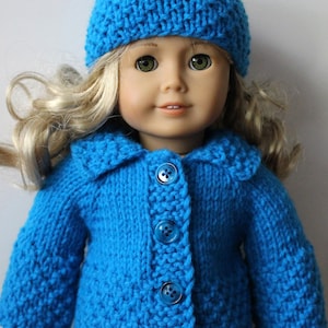 May include: A blue knitted cardigan with a matching blue knitted hat. The cardigan has a collar and buttons down the front. The doll is wearing the cardigan and hat.