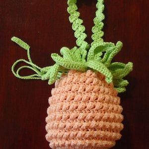 May include: A crocheted pineapple-shaped bag with a green top and a peach-colored body. The bag has a green crocheted strap.