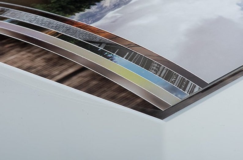 May include: A close-up of a white photo album with a curved edge. The album is open to reveal a series of colorful photographs.