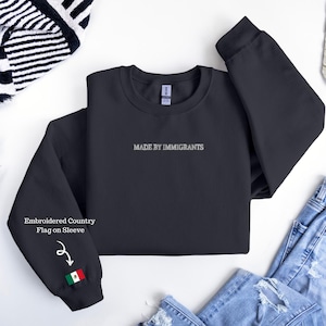May include: A dark gray sweatshirt with the text "MADE BY IMMIGRANTS" embroidered in white. The left sleeve features an embroidered Mexican flag. The words "Embroidered Country Flag on Sleeve" are also visible.