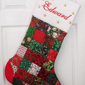 May include: A red and green patchwork Christmas stocking with the name "Edward" embroidered in red on the white cuff. The stocking is decorated with gold stars.