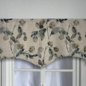 Op de afbeelding: Een beige valance met een aquarel bloemenpatroon in grijstinten en bruin. De valance heeft een gebogen onderrand en hangt boven een raam.