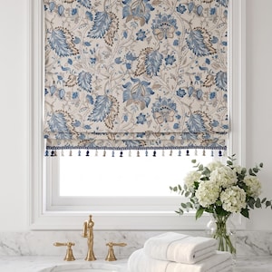 May include: A Roman shade window treatment featuring a cream background with a dense botanical pattern in shades of blue and brown. The bottom edge is finished with a decorative trim of small, alternating blue and white hanging tassels.