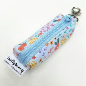 May include: A small blue zippered pouch with a floral print and a silver keychain. The pouch has a white label with the text "hollyberry" and "hollyberrydesigns.etsy.com".