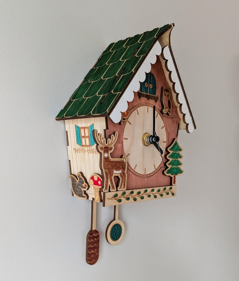 May include: A wooden cuckoo clock shaped like a house with a green roof, white trim, and a brown base. The clock face has a deer, squirrel, and mushroom design. The clock has a pendulum and a cuckoo bird.