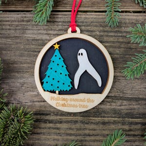 May include: Wooden Christmas ornament with a red ribbon. The ornament features a teal Christmas tree with a gold star and a white ghost on a black background. The text "Walking around the Christmas tree" is below the image.