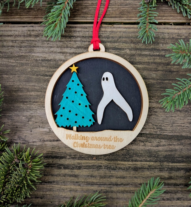May include: Wooden Christmas ornament with a red ribbon. The ornament features a teal Christmas tree with a gold star and a white ghost on a black background. The text "Walking around the Christmas tree" is below the image.
